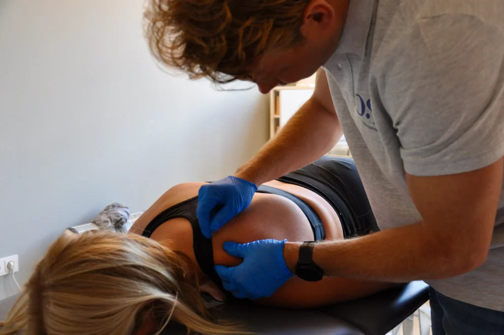 Osteopaat behandelt schouder van vrouw liggend op behandelbank met blauwe handschoenen
