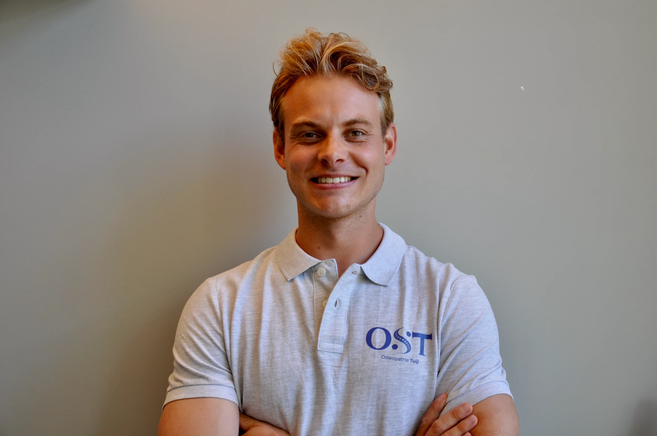 Osteopaat Niels Tuijl glimlacht en draagt een wit poloshirt met het logo van Osteopathie Tuijl